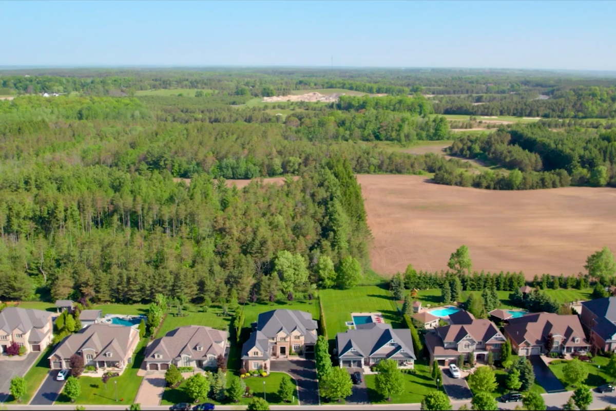 A high-resolution aerial view of a neighbourhood in Uxbridge surrounded by forests, trails, and rolling landscape, showing the natural setting buyers love in the NorthSide 
